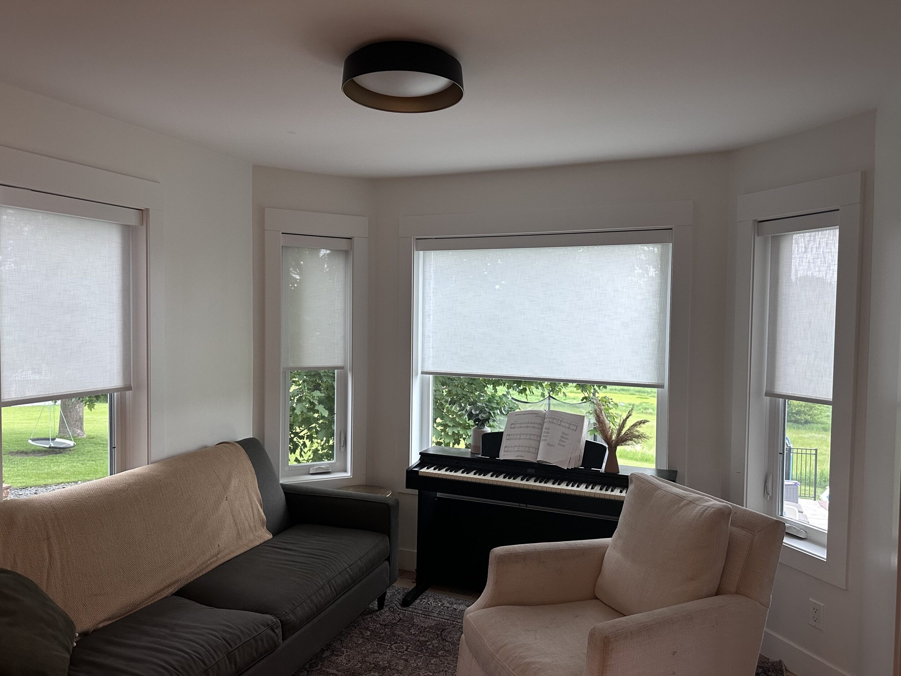A cozy living room with a couch, armchair, and piano near windows.